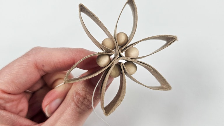 Die beiden Fadenenden sind nun nebeneinander. Die Schnur so lange festziehen, bis die Holzperlen ohne Abstand zueinander einen Kreis bilden. Die Schur auf Spannung halten und einen sehr engen Knoten machen.