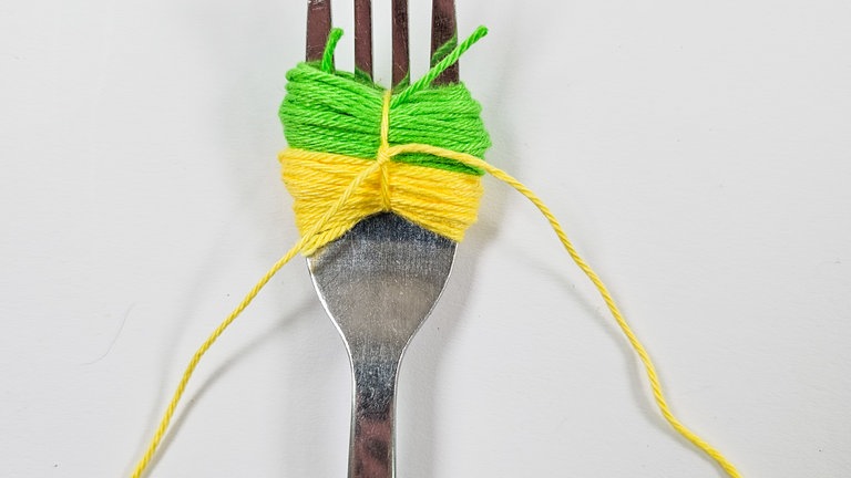 Nun die zuvor eingelegte Schnur nach vorne ziehen und sie so fest wie möglich um das Garnpaket verknoten.