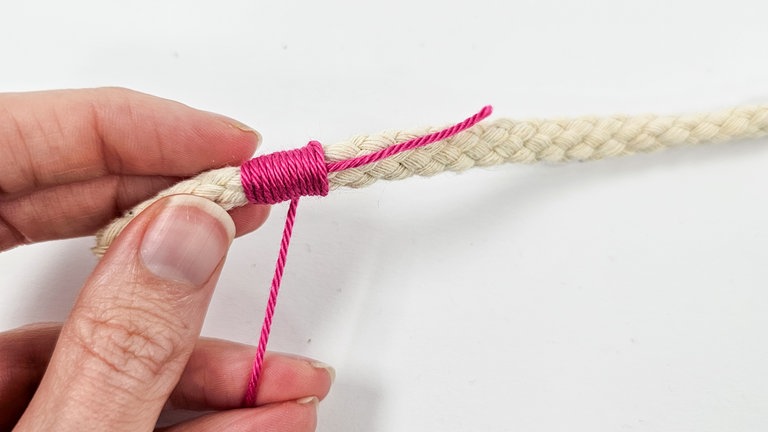 Das kurze Fadenende längs am Seil anlegen und nun Seil und Restfaden gemeinsam mit dem Garn umwickeln.