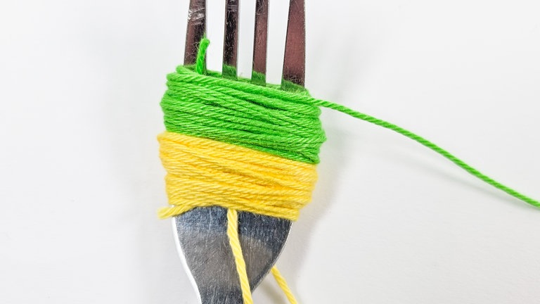 Das erste Garn abschneiden und die zweite Farbe mit ähnlich vielen Runden direkt darüber wickeln.