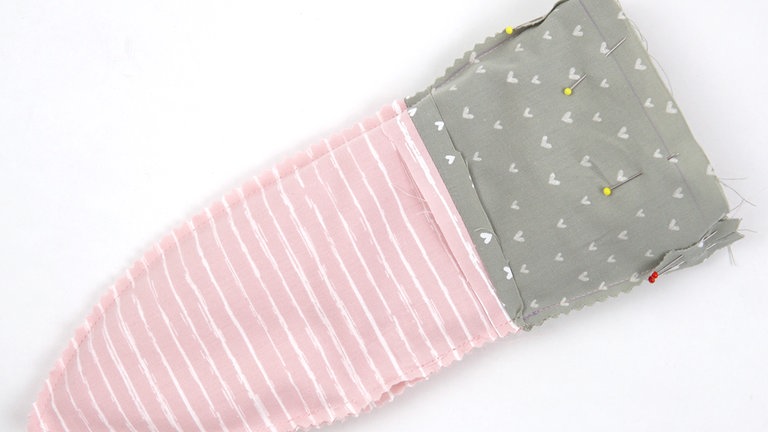 Das Außenteil auf rechts wenden und rechts auf rechts in das Innenteil schieben. Die obere Kante aufeinanderheften, dabei treffen die auseinandergebügelten Nahtzugaben an den Seitennähten aufeinander. 