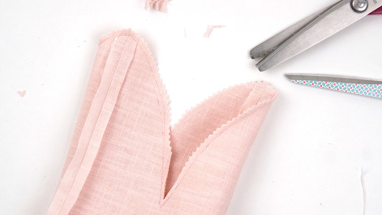 Die Ohrenkanten durchgehend aufeinandersteppen. Dann die Nahtzugaben auf ca. 5 mm zurückschneiden, in den Rundungen v-förmig einschneiden (oder eine Zickzackschere benutzen). 