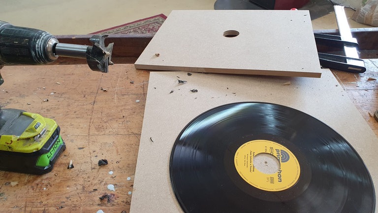 Schallplatte auf eine der beiden Holzplatte legen. Den Forstnerboher in den Akkuschrauber einspannen. In die andere MDF-Platten in der Mitte ein Loch bohren.