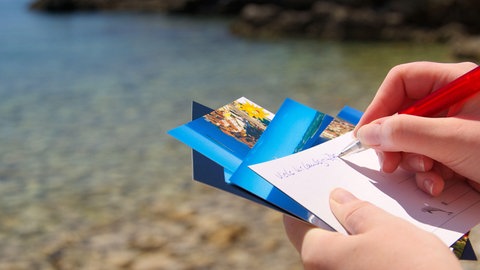Eine Frau schreibt am Strand Postkarten.