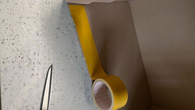 Im Karton (Innenseite, oberer Rand) wird an allen 4 Seiten das doppelseitige Klebeband 4cm breit angebracht. Es hält den Umschlag nach innen fest.