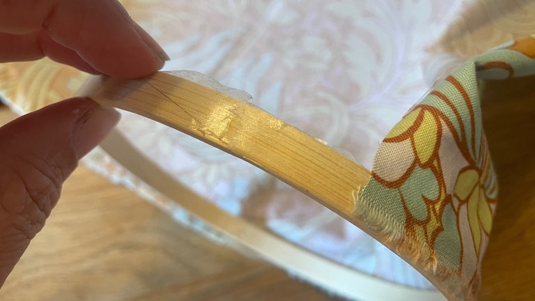 Den inneren Ring des Stickrahmens außen entlang mit dem doppelseitigen Klebeband versehen. Das Papier abziehen und den Stoff mit der langen Kante ringsherum festkleben. 