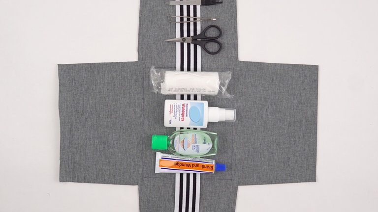 Legen Sie das Schnittteil aus Innenstoff mit der rechten Stoffseite nach oben vor sich. Die Erste-Hilfe-Utensilien zunächst einmal auf dem Gummiband anordnen. 