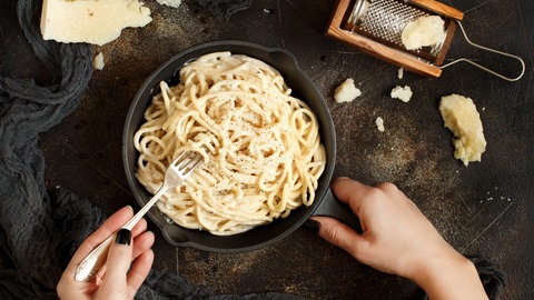 Ein Teller mit dem Pasta-Gericht Cacio e Pepe, daneben ein Stück Käse mit einer Reibe.