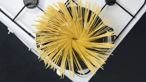 Noch feste Spaghetti die gerade in einen Topf kochendes Wasser gegeben wurden. Für das Pasta-Gericht Cacio e Pepe ist Stärke im Wasser unverzichtbar.