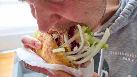 Mann isst Fastfood: Binge-Eating beginnt meistens später als Magersucht, sie betrifft vor allem junge Erwachsene. Diese Essstörung ist durch immer wiederkehrende Essanfällen gekennzeichnet. Im Unterschied zur Bulimie versuchen die Betroffenen in der Regel nicht, eine Gewichtszunahme durch Erbrechen zu verhindern.