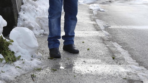 Eine Person steht auf einem vereisten Gehweg, tags: Glatteis Sturz schützen