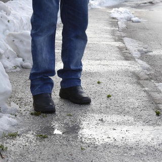 Eine Person steht auf einem vereisten Gehweg, tags: Glatteis Sturz schützen