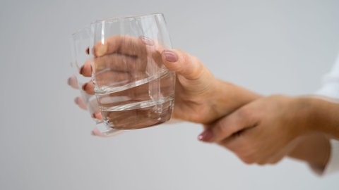 Verwackelte Hand mit Tremor hält Wasserglas.