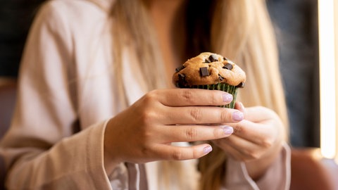 Einsamkeit könnte das Essverhalten verändern: Das Verlangen nach süßem Essen wird höher | Eine Frau hält einen Muffin.