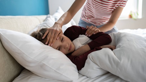 Kind liegt krank im Bett. Forscher haben das Rätsel um das Entzündungssyndrom gelöst, das bei Kindern nach einer Infektion mit Corona auftreten kann.