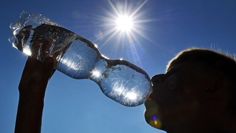 Ein Mann trinkt bei strahlender Sonne aus einer Wasserflasche.