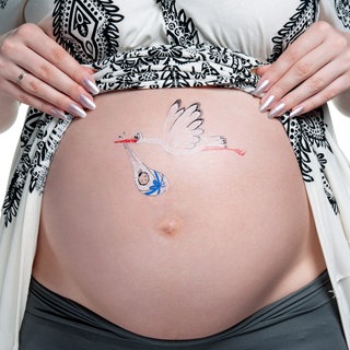 Bauch einer schangeren, darauf gemalt ein Storch, der ein Baby bringt, das in weiße Tücher verpackt ist, die mit einem blauen Band gehalten werden: Es gibt sehr viele Mythen oder Ammenmärchen in Bezug auf die Schwangerschaft. Sehr viele davon beschäftigen sich mit der Prädiktion, also mit der Vorhersage des Geschlechts.