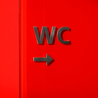 Hinweisschild zur Toilette auf rotem Untergrund: Das Thema Reizblase tritt typischerweise nach der letzten Regelblutung auf – in der Phase, in der der Östrogenspiegel ganz niedrig ist. Von Anneliese Schwenkhagen