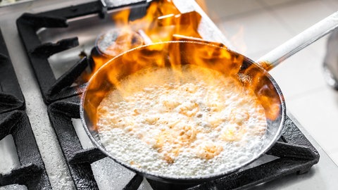 In einer Pfanne auf dem Herd wird ein Gericht flambiert: Viele fragen sich, ob beim Kochen und Backen der Alkohol verdampft oder ob Reste bleiben, die für Kinder und trockene Alkoholiker problematisch sind
