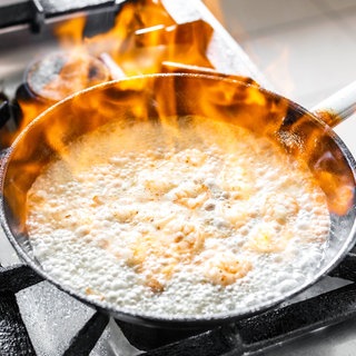 In einer Pfanne auf dem Herd wird ein Gericht flambiert: Viele fragen sich, ob beim Kochen und Backen der Alkohol verdampft oder ob Reste bleiben, die für Kinder und trockene Alkoholiker problematisch sind