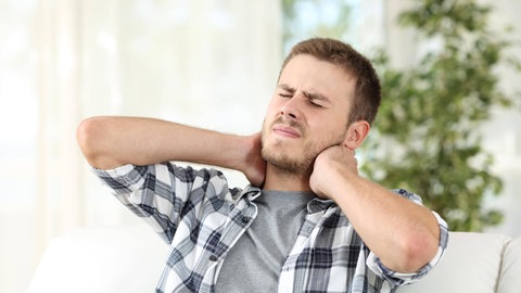 Junger Mann hält sich mit schmerzverzerrtem Gesicht den Nacken: Die internationale medizinische Definition sagt: "Schmerz ist immer subjektiv." Daher kann man von außen niemals beurteilen, welche Schmerzen ein Mensch hat.