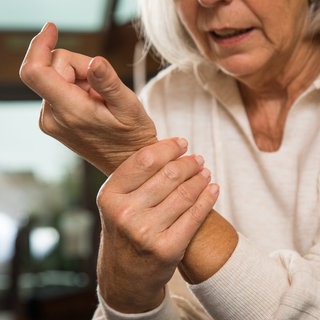 Ältere Frau hält sich das schmerzende Handgelenk: Leider gelingt es an keinem Arthrosegelenk, die Arthrose zu heilen oder die Gelenke in einen Zustand zu bringen, in dem sie in der Jugend waren. Aber es gibt bei der Fingergelenksarthrose und an den Handgelenksarthrosen sowohl konservative als auch operative Maßnahmen, die dem Patienten eine Linderung verschaffen.