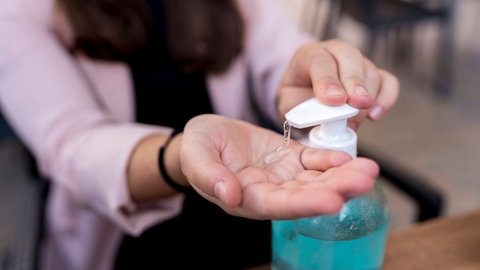 Frau desinfiziert sich die Hände an einem Desinfektionsmittelspender: Händedesinfektion ist wichtig, um sich vor dem Coronavirus zu schützen