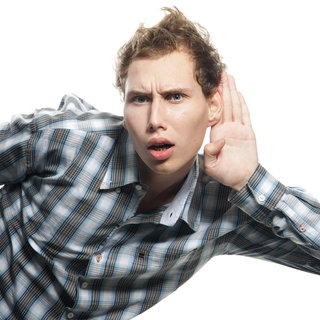 Ein junger Mann hört schlecht und legt die Hand hinters Ohr: In einer lauten Umgebung, einer Bar oder einem Restaurant fällt es auf, wenn man andere nicht mehr gut versteht. Öfter nachfragen oder andere noch mal ansprechen zu müssen sind Anzeichen für eine beginnende Schwerhörigkeit. 