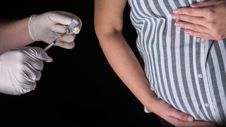 Eine Person mit Schutzhandschuhen indiziert mit einer Impfspritze eine Impfdosis mit dem mRNA-Impfstoff Comirnaty von Biontech: Influenza-, Pertussis- und Covid-19-Impfung sind von der STIKO für Schwangere empfohlen