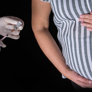 Eine Person mit Schutzhandschuhen indiziert mit einer Impfspritze eine Impfdosis mit dem mRNA-Impfstoff Comirnaty von Biontech: Influenza-, Pertussis- und Covid-19-Impfung sind von der STIKO für Schwangere empfohlen
