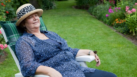 Eine Seniorin mit Sonnenhut hält im Garten ein Mittagsschläfchen