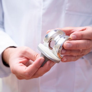 Ein Arzt hält eine Knieprothese in den Händen. Solche künstlichen Kniegelenke, die z. b. bei Arthrosepatienten zum Einsatz kommen müssen oft nach rund zehn bis 15 Jahren ausgetauscht werden. Eine längere Haltbarkeit erhoffen sich Mediziner durch neue Werkstoffe und neue operative Zugangswege.