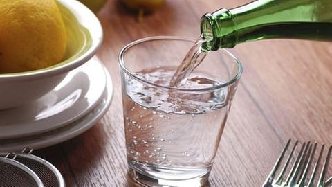 Mineralwasser wird in ein Glas an einem gedeckten Tisch aus einer Glasflasche eingeschenkt.