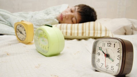 Frau schläft vor drei Weckern. Für einen optimalen Mittagsschlaf mit Geistesblitz sollte man sich den Wecker stellen. Der Schlaf darf nicht zu lange dauern, sonst ist man beim Aufwachen wieder müde.