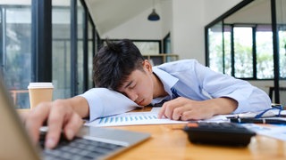 Mann schläft am Arbeitsplatz. Ein Mittagsschlaf macht schlauer und verhilft zu einem Geistesblitz, so eine neue Studie.