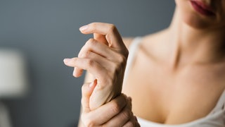 Eine Frau hält sich die Handgelenke - Handgelenks-Übungen können bei Karpaltunnelsyndrom helfen