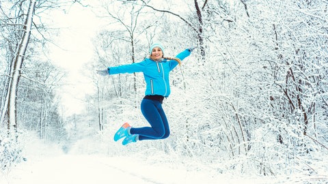 Frau springt in Schneelandschaft in die Luft