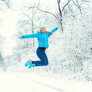 Frau springt in Schneelandschaft in die Luft