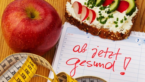 Kalender mit den Worten "Gesunde Ernährung" mit Maßband, Obst und Brot