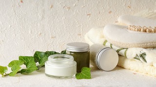 Efeuranke mit Salbe und Schraubglas daneben ein Handtuch und eine Anti-Celluliteschwamm