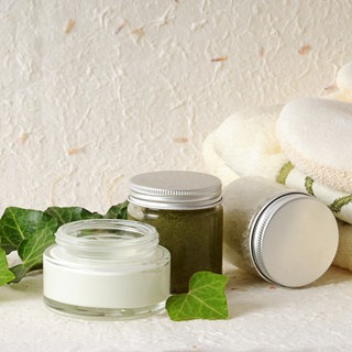Efeuranke mit Salbe und Schraubglas daneben ein Handtuch und eine Anti-Celluliteschwamm