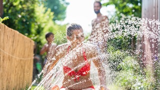 Frau sitzt vor Wassersprenger