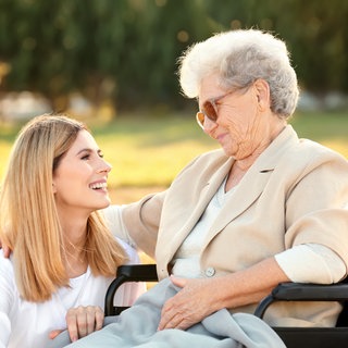 Jüngere Frau unterhält sich mit älterer Frau im Rollstuhl