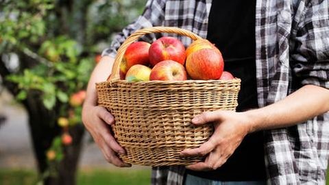 Ein Mann hält einen Korb mit Äpfeln.