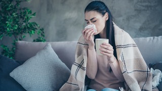 Frau sitzt mit einer Erkältung auf der Couch