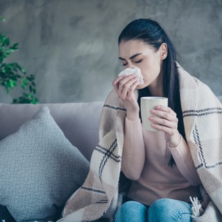 Frau sitzt mit einer Erkältung auf der Couch