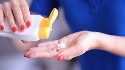 Frauenhand holt Sonnenschutz für die Haut