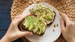 Brot belegt mit Frischkäse und Avocado und bestreut mit Kürbiskernen und Sesam.