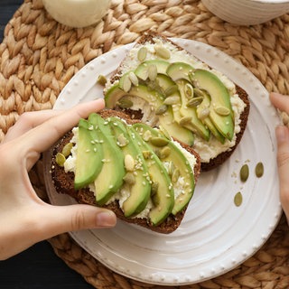 Brot belegt mit Frischkäse und Avocado und bestreut mit Kürbiskernen und Sesam.