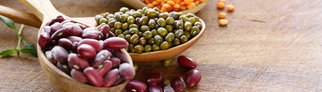 Kichererbsen, rote Linsen, Mungbohnen und Kidneybohnen liegen auf Holzlöffeln auf einer Platte. Wie gesund sind Hülsenfrüchte?